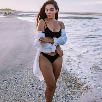 foto de uma mulher de nome Thainá na praia de Parajuru ela está em pé de biquini preto com uma blusa branca e o sol acabou de se pôr